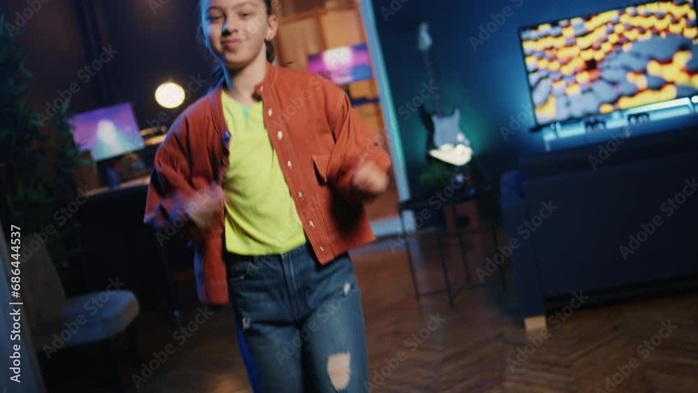 Dutch angle shot of cute girl in neon lit apartment filming dance tutorial for other children watching her online social media content. Kid in home studio recording video entertaining gen Z viewers Dutch angle shot of cute girl in neon lit apartment filming dance tutorial for other children watching her online social media content. Kid in home studio recording video entertaining gen Z viewers