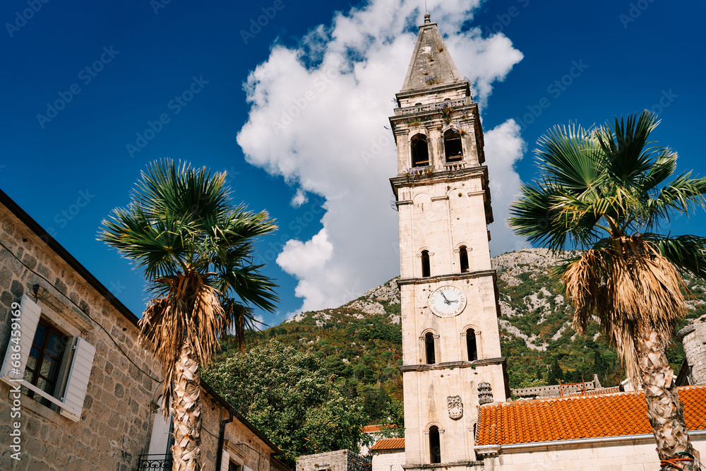 Bell tower of the Church of St. Nicholas with a clock among ancient houses against the backdrop of green mountains. Perast, Montenegro