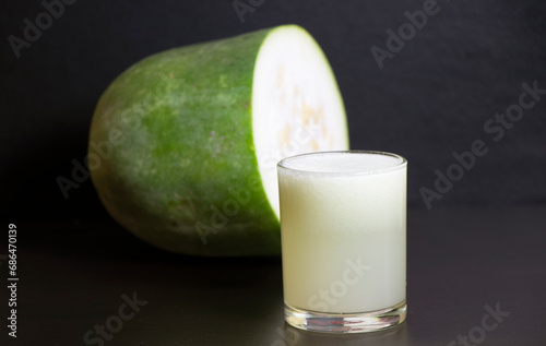 A glass of Ash gourd Juice in focus with Raw ash gourd in background.