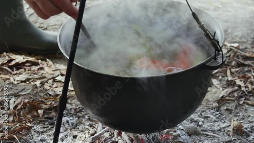 stirring fish soup with a ladle, cooking fish soup in a cauldron over a fire in nature