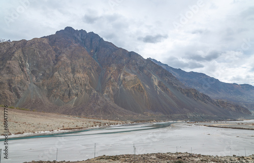 Valley between mountains on a cloudy day. A Dried river trains of Shyok river in Nubra Valley in Ladakh Region of Indian Himalayan territory .A  Barren landscape of Cold dessert in Himalaya Valley . photo