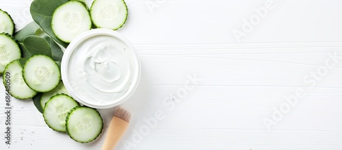 Cooling face mask with eucalyptus leaves, brush, and fresh cucumber slices on white table. Ethical botanical skincare. photo