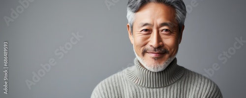 portrait of mature asian man in grey knitted sweater on grey background. copy space, banner photo