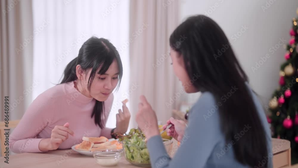 Asian female friends joyfully prepare a salad and savor it at the dining table in the festive atmosphere of Christmas at her home, the happiness of holiday celebrations. Asian female friends joyfully prepare a salad and savor it at the dining table in the festive atmosphere of Christmas at her home, the happiness of holiday celebrations.
