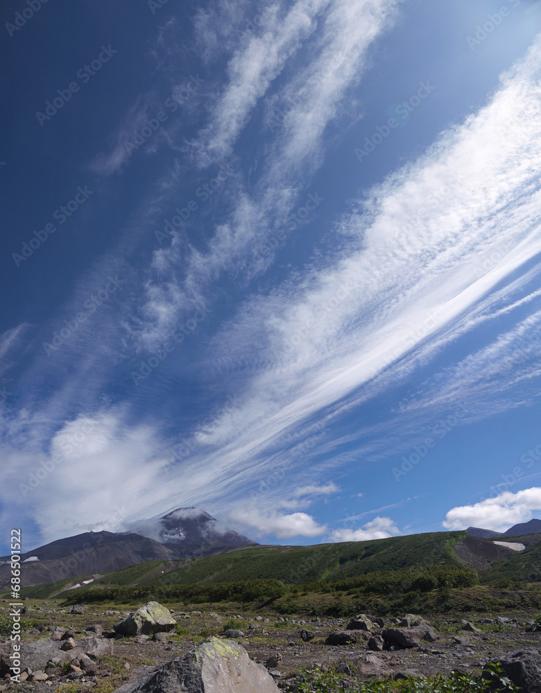 Kozelsky Volcano with mountain top obscured by dramatic Cirrus clouds on clear blue sky and valley view on sunny day, Avachinsky pass on Kamchatka