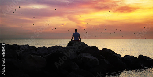 Silhouette of a man sitting on a rock and watching the sunset © Grey Zone