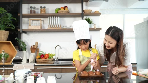 Small girl enjoying making cake with her mother in kitchen at home