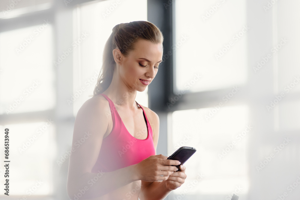 Smiling young sporty woman using mobile phone and typing sms, Happy athletic lady texting on cellphone, wearing a smile. Smiling young sporty woman using mobile phone and typing sms, Happy athletic lady texting on cellphone, wearing a smile.