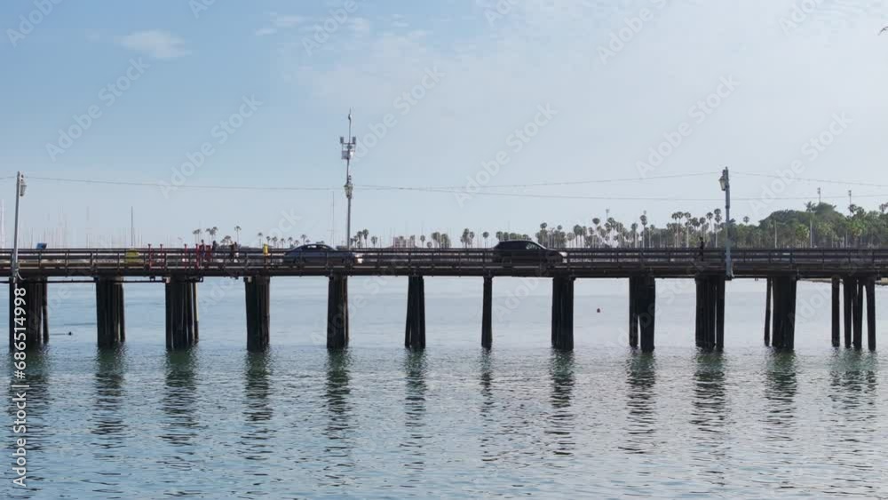Daytime view of cars driving on the Stearns Wharf, Santa Barbara, California, USA. Tourists walking on old wooden pier over waters of Pacific Ocean. Stearns Wharf popular tourist attraction in city Daytime view of cars driving on the Stearns Wharf, Santa Barbara, California, USA. Tourists walking on old wooden pier over waters of Pacific Ocean. Stearns Wharf popular tourist attraction in city