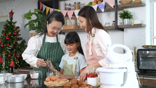 Three generations Asian women in apron enjoy baking together in kitchen room at home. Grandmother, mother and little daughter helping baking together.