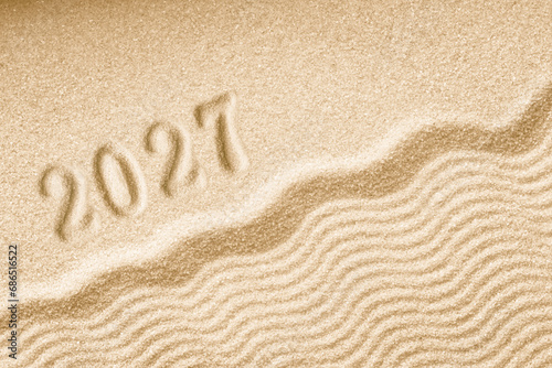 Imprints of numbers 2027 happy new year on a golden sand waves