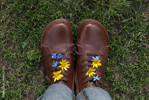 women's brown leather boots on grass. Blue and yellow flowers stick out among laces. spring walk for pleasure, energy of nature, freedom , active lifestyle. view from above. Hi spring. Earth Day