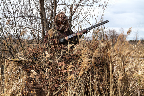 A duck hunter stands in a camouflaged hideout photo