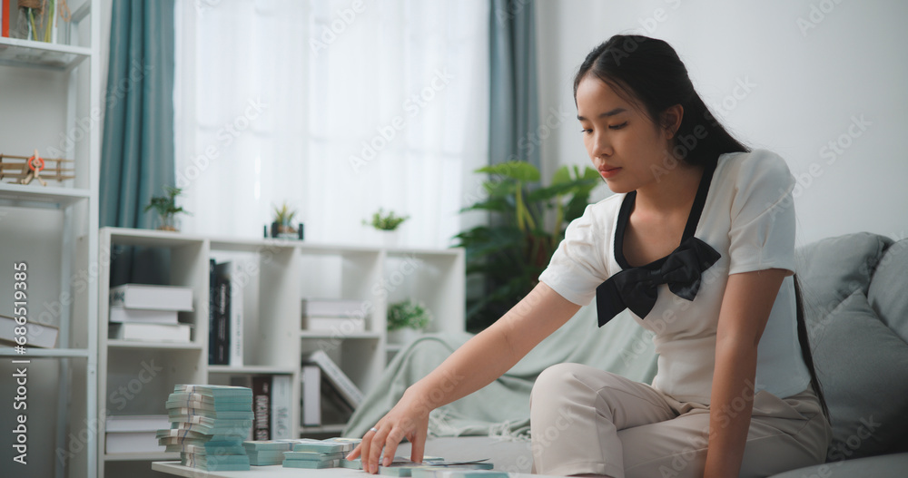 Fototapeta premium Portrait of Happy young asian woman counts cash dollar bills while sitting in living room at home,counting stack cash money dollar