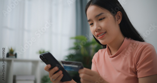 Portrait of Young asian woman sitting on sofa in living room, makes online banking payments through the internet from bank card on smartphone ,Shopping online with credit card.