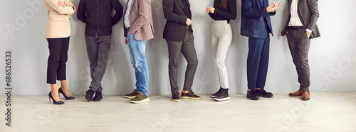 Legs of different business people standing in row and communicating with each other. Unrecognizable people in stylish business and smart casual clothes stand on wall background. Banner. Cropped image.