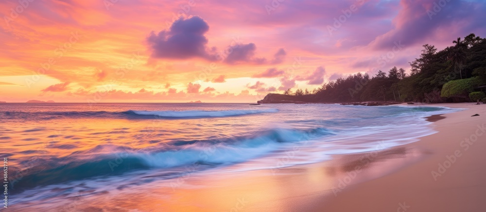 Obraz premium Colorful sunset over the sea with pink, purple, and orange sky, yachts on the horizon, and foamy waves on a sandy beach in Seychelles' Mahe.
