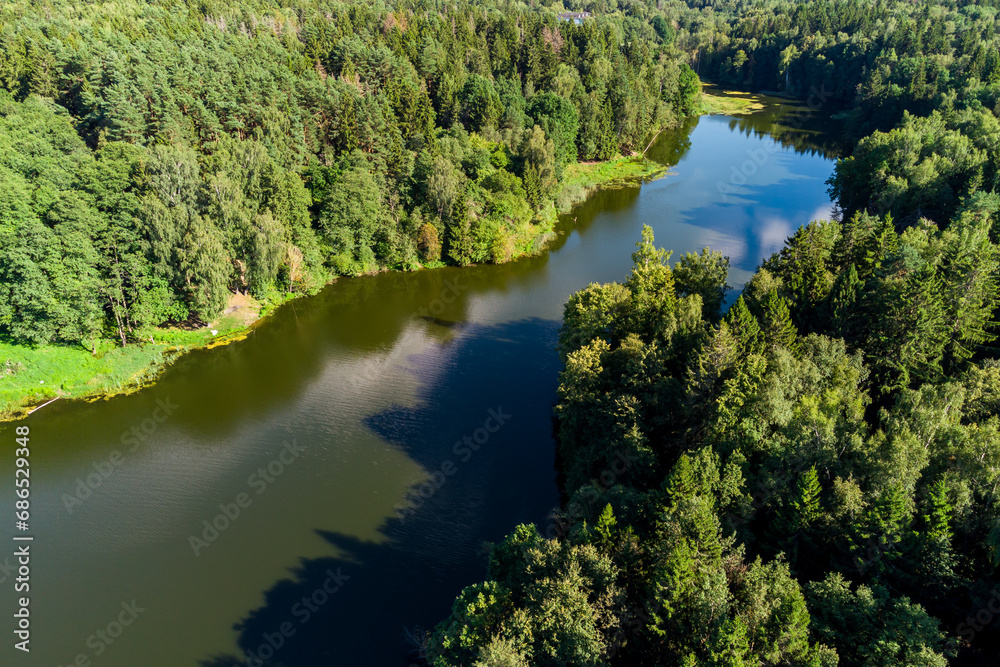 An elongated pond surrounded by dense forest. Pond on the Stradalovka River, Balabanovo, Russia