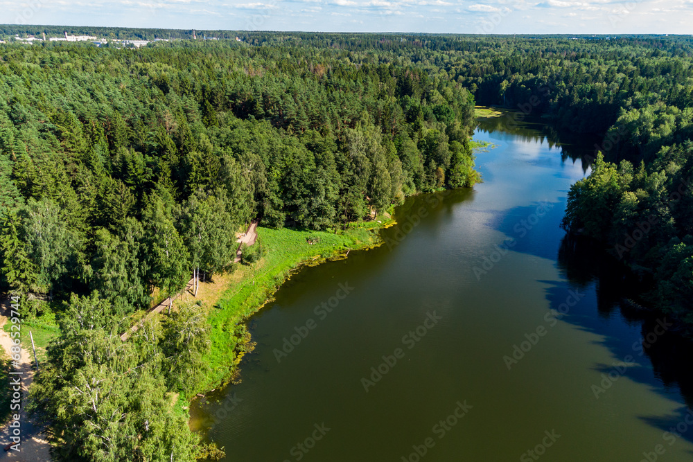 A picturesque elongated pond surrounded by forest and a walking area on the shore