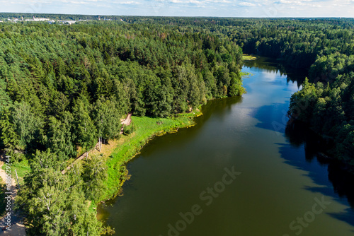 A picturesque elongated pond surrounded by forest and a walking area on the shore