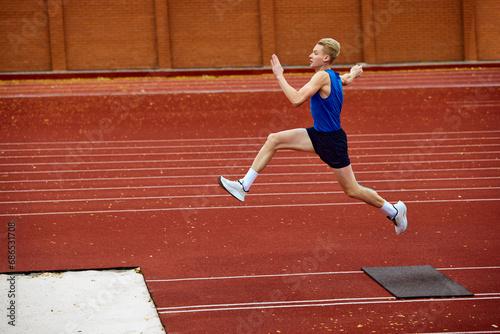 Intensity of effort visible in mid-air jump. Young attractive sportsman jumps from point to make a perfect long jump to sand.