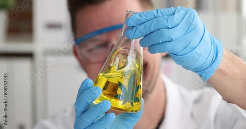 Man scientist chemist shaking yellow marijuana oil in flask 4k movie slow motion. Pharmaceutical production of narcotic drugs concept