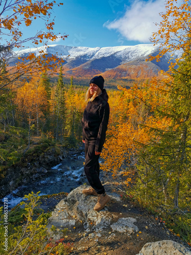 A girl on the background of an autumn Arctic landscape in the Khibiny mountains. Kirovsk, Kola Peninsula, Polar Russia. Autumn colorful forest in the Arctic, mountain hikes and adventures.