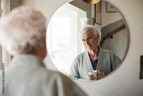 Senior man holding coffee cup while looking in mirror at home photo