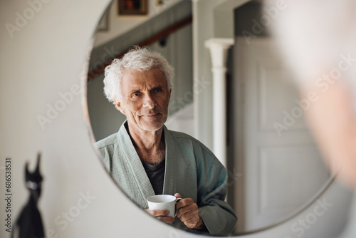 Smiling senior man with coffee cup looking at himself in mirror at home
