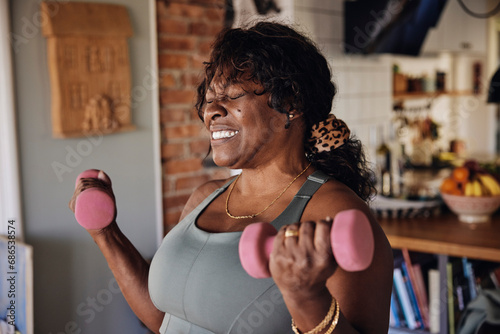 Mature woman with eyes closed clenching teeth while exercising with dumbbells at home photo