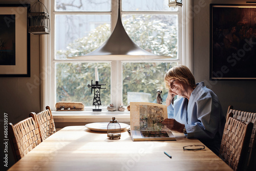 Smiling senior woman looking at picture book on dining table at home photo