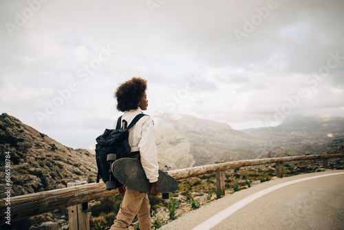 Young female backpacker walking on road holding skateboard during vacation photo