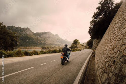Man riding motorcycle on road in front of mountains aganist sky photo