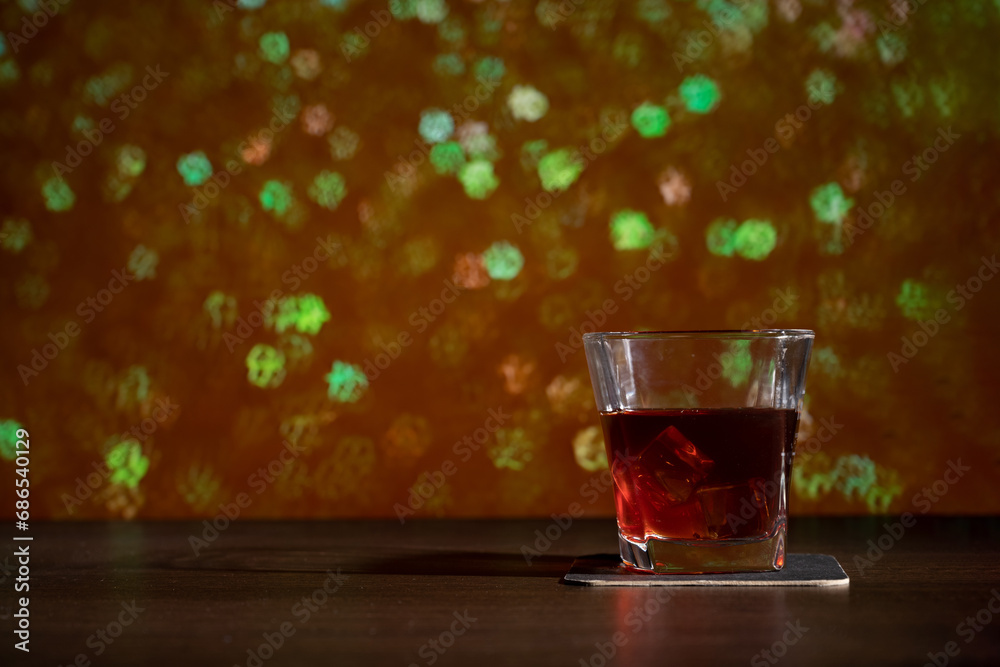 Glass of whiskey on the bar in front of the blur image Christmas background. Festive abstract background with bokeh defocused lights and stars Glass of whiskey on the bar in front of the blur image Christmas background. Festive abstract background with bokeh defocused lights and stars