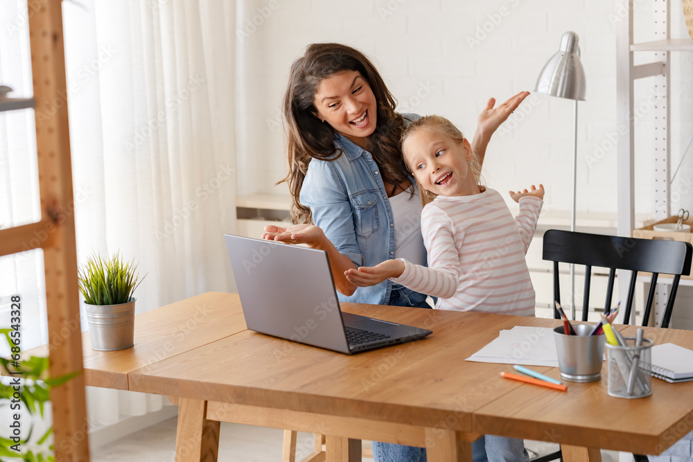A joyful mother and her adorable little girl are having a great time, dancing together in front of a laptop computer A joyful mother and her adorable little girl are having a great time, dancing together in front of a laptop computer