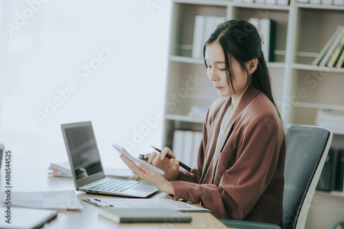 Two cute Asian businesswomen in suits talking in modern workplace. Thai woman. Southeast Asian woman. looking at laptop together in office