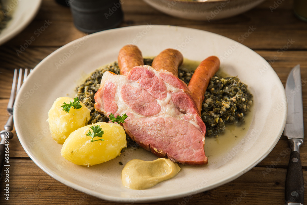 Oldenburger Grünkohl mit geräucherter Kohlwurst, Pinkel, Kassler Nacken, Kartoffeln, Senf, Petersilie auf Teller und Holz Hintergrund Oldenburger Grünkohl mit geräucherter Kohlwurst, Pinkel, Kassler Nacken, Kartoffeln, Senf, Petersilie auf Teller und Holz Hintergrund