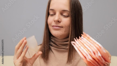 Smiling brown haired woman holding hygiene pads and menstrual cup making decision of hygienic products choosing alternative eco friendly variant of protection during period. photo