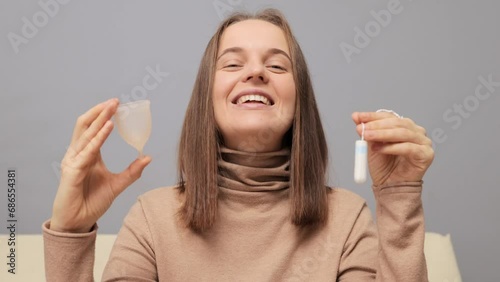 Intimate and safe health. Cheerful woman showing collector menstrual cup and tampon choosing protective products for using during menses nodding head in approval.