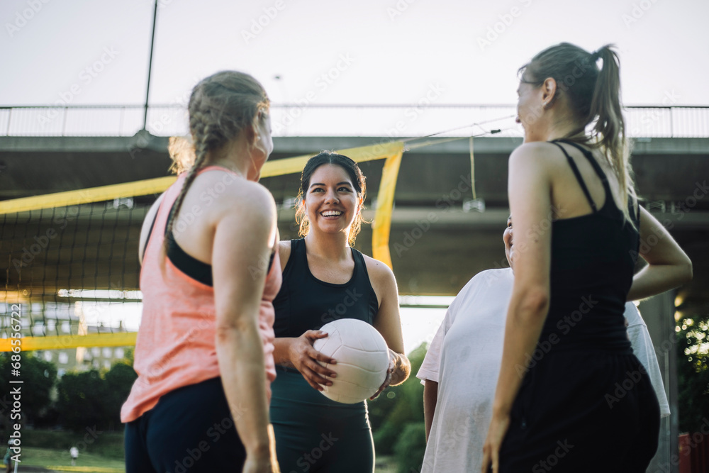 Low angle view of smiling woman holding volleyball with female friends Low angle view of smiling woman holding volleyball with female friends