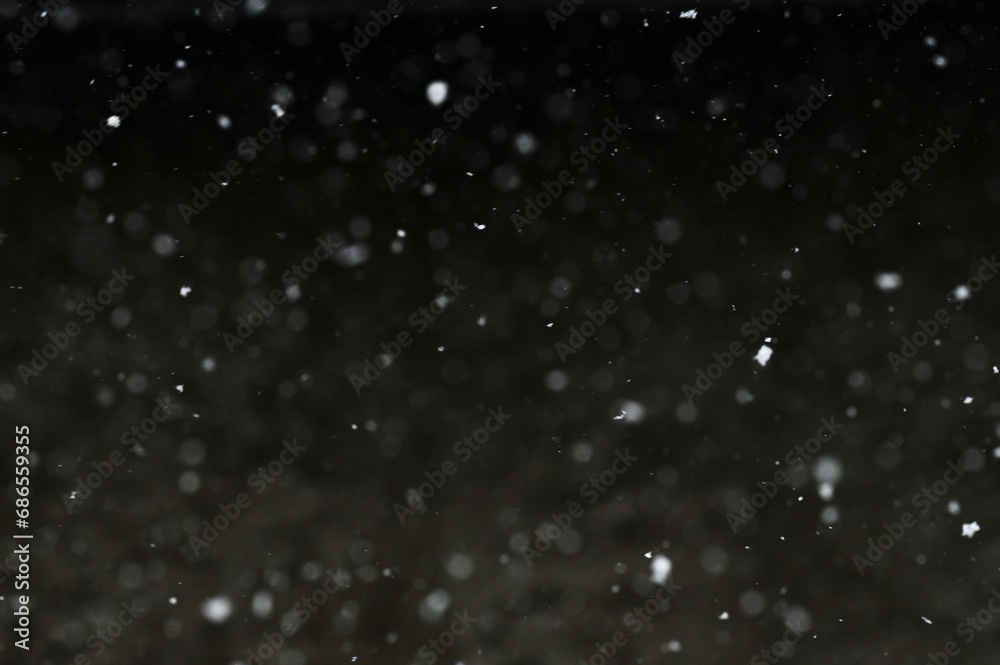 Bokeh of white snow on a black background. Falling snowflakes on night ...