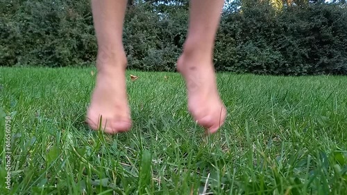 Happy child jumping on green grass in park barefoot. close-up legs of boy walking barefoot on lawn in summer. Happy childhood. Hardening, active healthy lifestyle. Bottom view photo