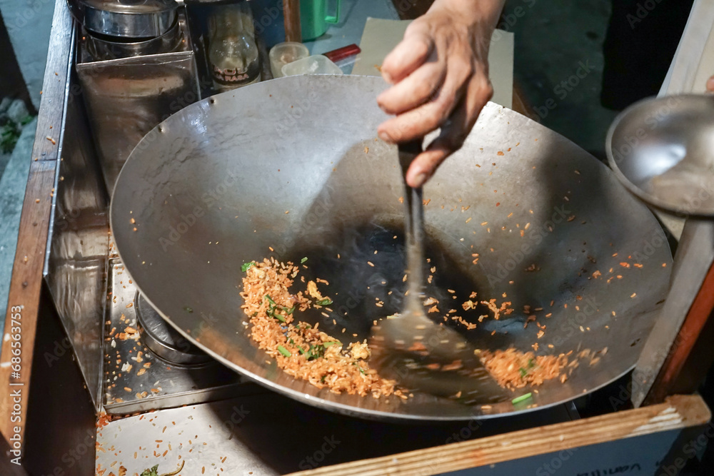 A man cooking fried rice on steel skillet pan for selling on the street food. Indonesian call the dish Nasi Goreng. Indonesian Street food culinary A man cooking fried rice on steel skillet pan for selling on the street food. Indonesian call the dish Nasi Goreng. Indonesian Street food culinary
