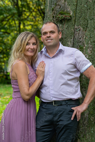 Portrait of a romantic, loving couple. A man and a woman are standing near a large tree. A woman in a beautiful pink dress. A happy family