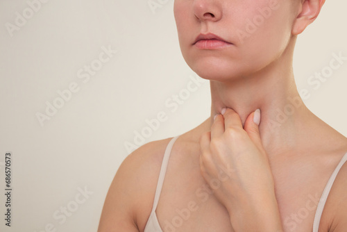 a young Caucasian brunette woman holds her hand on her neck, suffers from a sore throat, experiences pain when swallowing, loss of voice, thyroid disease.