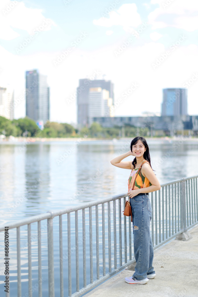 A positive expression in nature's embrace cute girl in an orange shirt stands on a bridge overlooking the water. A positive expression in nature's embrace cute girl in an orange shirt stands on a bridge overlooking the water.