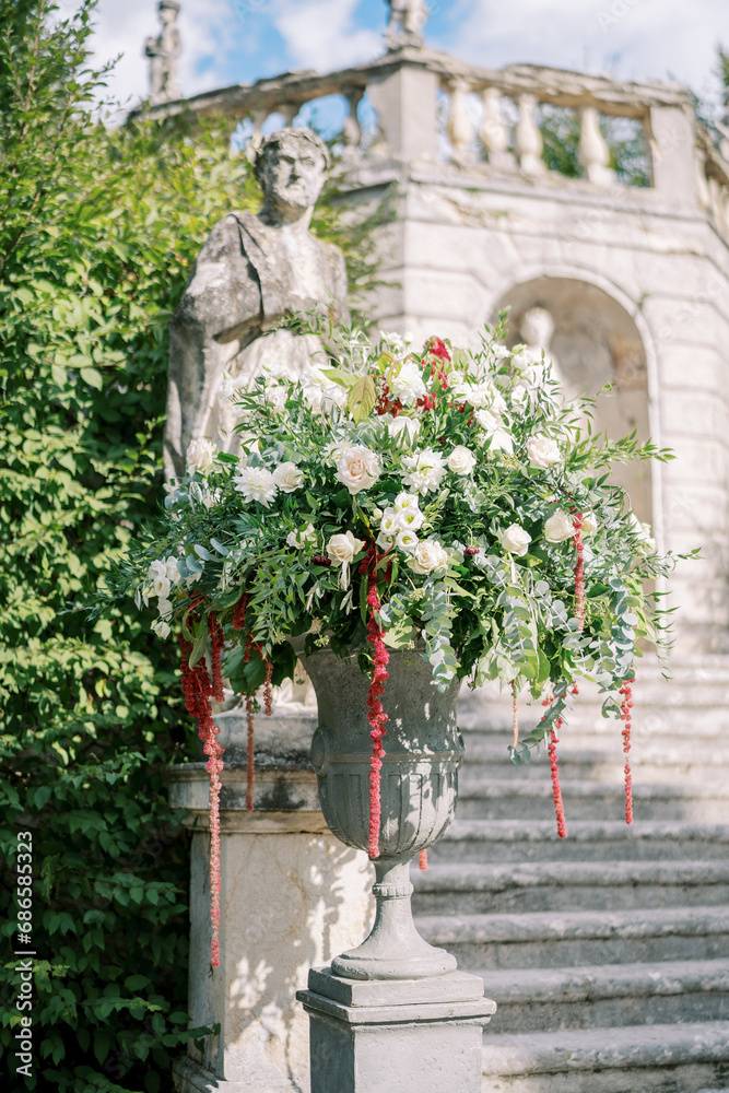 Bouquet of flowers stands in a stone vase near a statue in a green garden