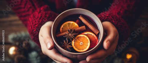 Female hands holding a cup of hot mulled wine with spices on a background.