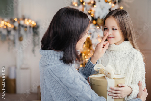 Mother affectionately touching her daughter's nose on Christmas, with gifts.