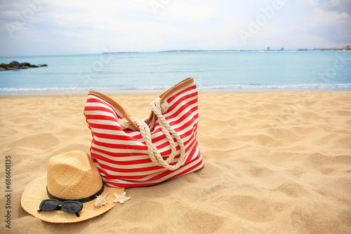 Fototapeta Naklejka Na Ścianę i Meble -  Stylish striped bag with straw hat, sunglasses, seashell and starfish on sandy beach near sea. Space for text